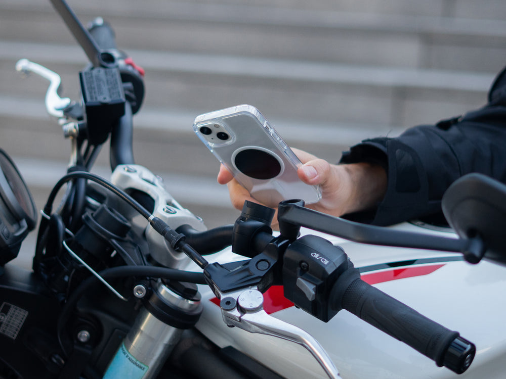 Motard fixant son smartphone sur le support téléphone moto pro avec plaque monté sur le guidon de sa moto. Le support magnétique assure une fixation sécurisée et rapide, idéal pour la navigation et l’utilisation du téléphone en toute sécurité sur la route.